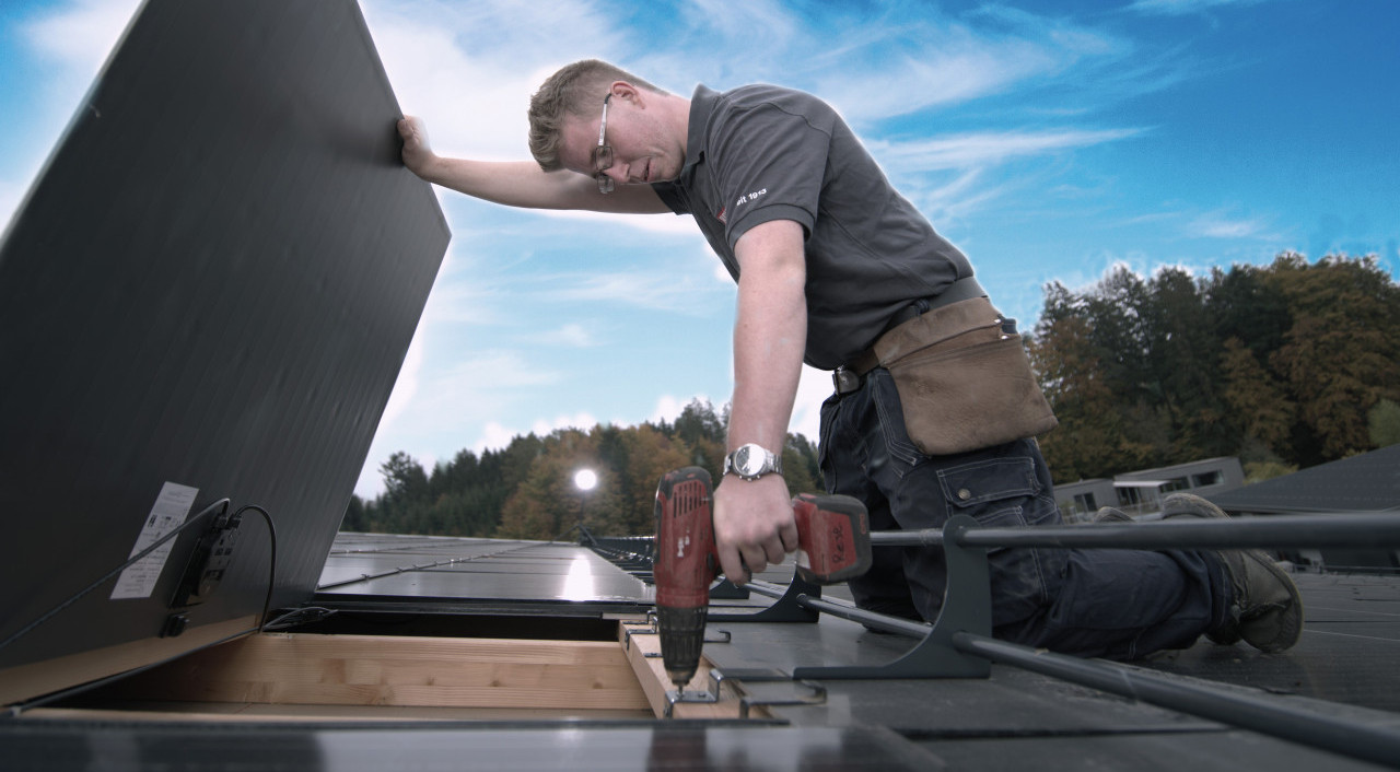Person installiert eine Solaranlage auf einem Dach bei Gebäudehülle Schweiz